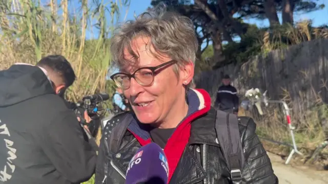 A woman in a black leather jacket with short hair speaks into a microphone