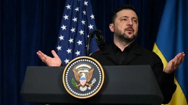 Zelensky speaking at a podium with his hands outstretched to make a point