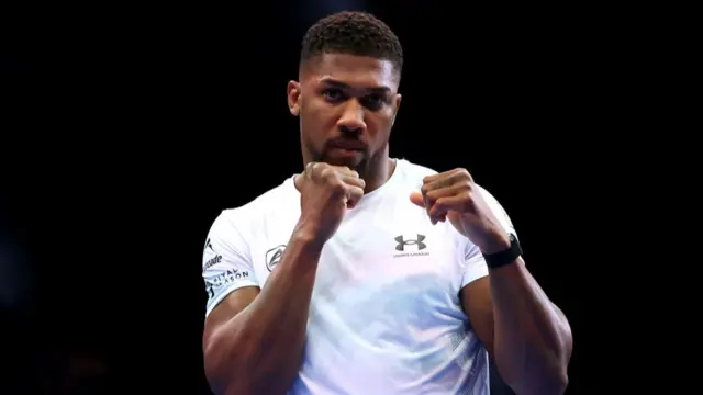 Anthony Joshua in a white t-shirt holding a boxing stance without gloves during a training session