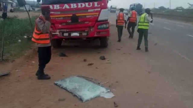 Officials stand near a truck, with what looks like a shattered windscreen on the floor