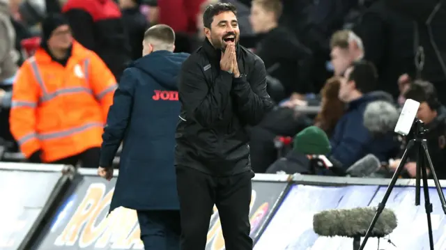 Swansea boss Vitor Matos smiles and clasps both hands in a prayer gesture