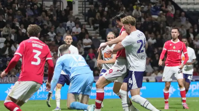 Wrexham striker Kieffer Moore scoring against Preston while under pressure from Michael Smith with the goalkeeper diving towards Moore's feet