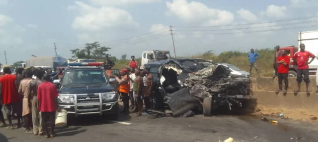 A police car with people crowded round it beside a wrecked car