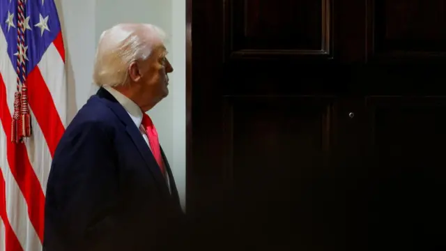 A side-on view of US President Donald Trump walking through an open door after a cabinet meeting.