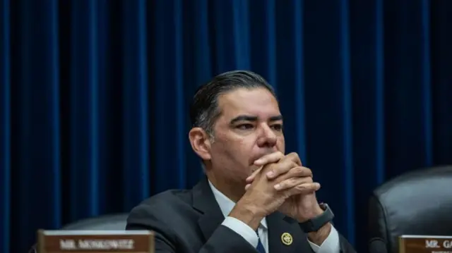 A man in a suit in front of a blue curtain