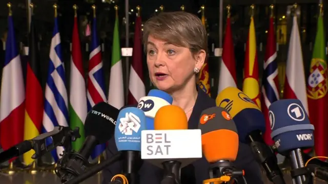 Yvette Cooper speaking infront of Nato flags and microphones