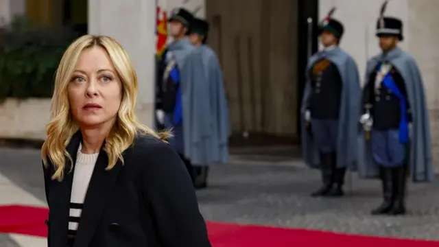 Italy’s Prime Minister Giorgia Meloni standing in the foreground, with guards in ceremonial dress behind her.
