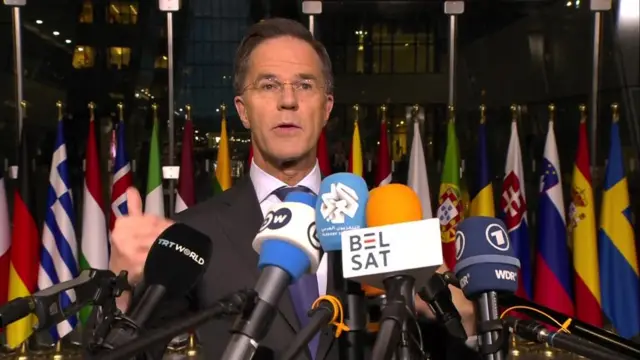 Rutte speaking into microphones in front of Nato flags