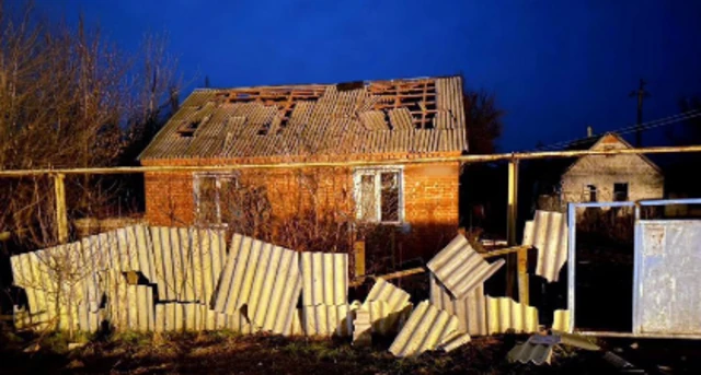 A broken fence outside a house with damage to its roof