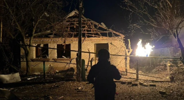 A house with a completely damaged roof and a fire besides it