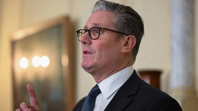A side-on view of a serious-looking Prime Minister Keir Starmer, who has his right hand and index finger raised.