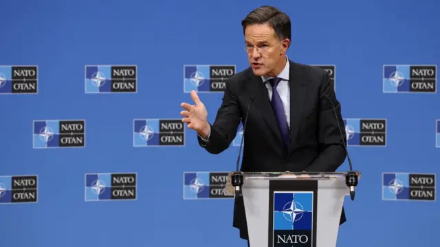 Mark Rutte gestures with his extended right hand while speaking from a Nato podium.