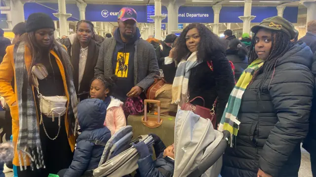 Eight members of the Ndukaeza family in warm winter clothing and with several bags