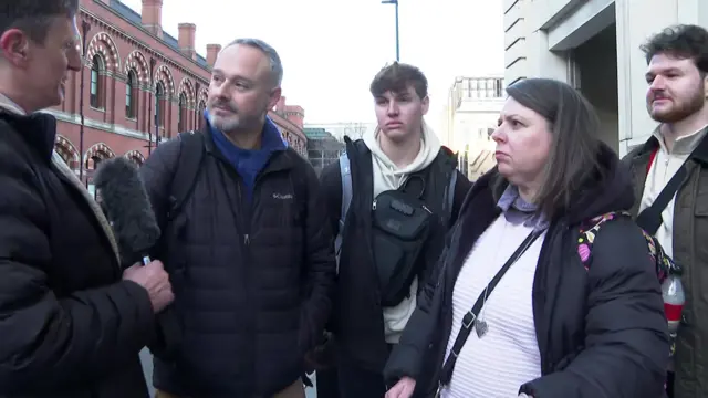 A couple and their two sons stand outside Kings Cross in black coats