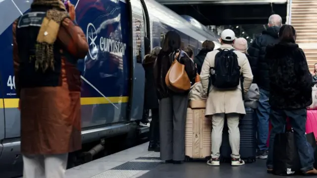 A group of people in thick winter coats stand with suitcases next to a train