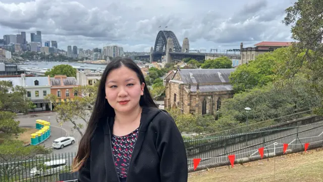 Kris Liu pictured wearing a black top with the backdrop of Sydney behind her