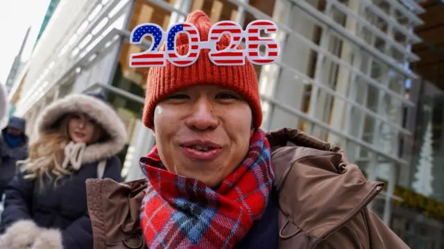A reveler on 6th Avenue poses for a photograph after waiting in line for hours to enter Times Square before New Year's Eve celebrations in the Manhattan borough of New York City.