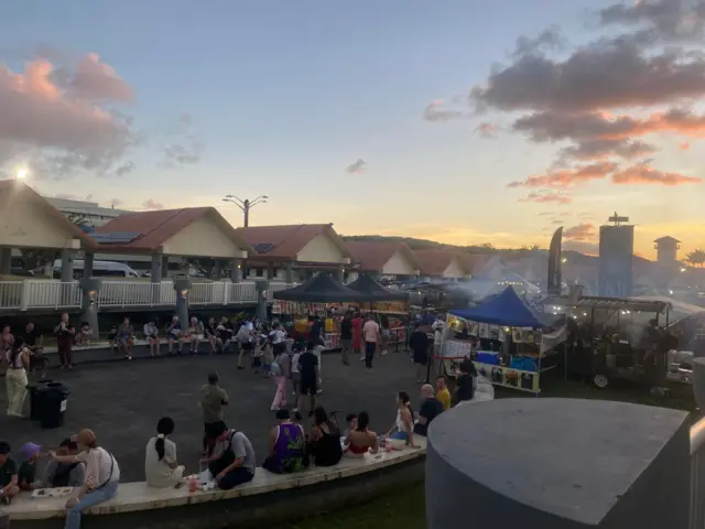People sit and eat on benches at sunset at a market on the island of Guam