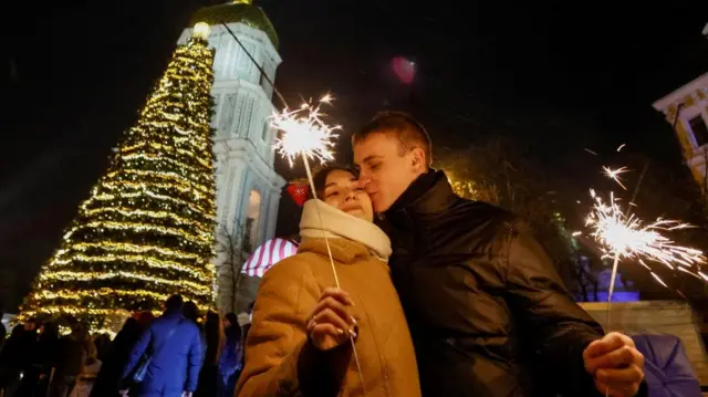A couple kisses next to a Christmas tree during a New Year's eve celebration before a curfew, amid Russia's attack on Ukraine, in Kyiv.