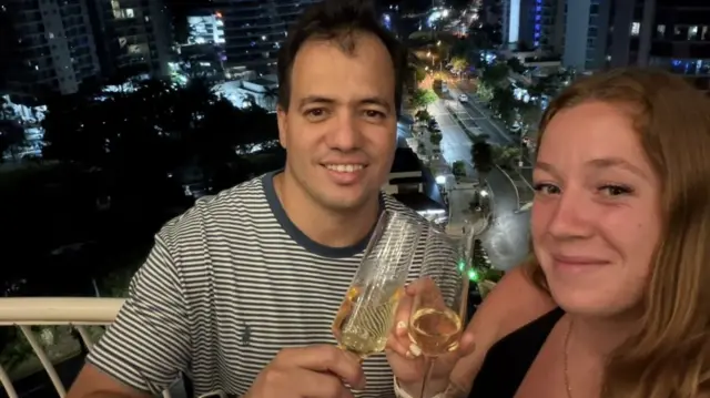 Marcondes and Megan holding champagne glassses - the road behind them is the state border