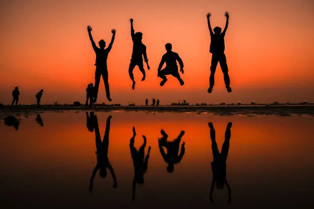 People are silhouetted while jumping during the last sunset of the year.