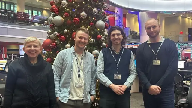Four BBC live page team members standing in front of a Christmas tree in the newsroom