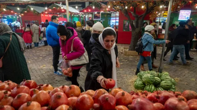 A woman picks up a pomegranate fruit from a pile