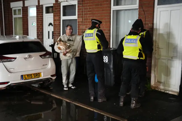 Man carrying dog talking to police outside house in Derby
