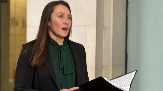 Vicky Evans wearing a dark green blouse and black blazer, reading a statement.