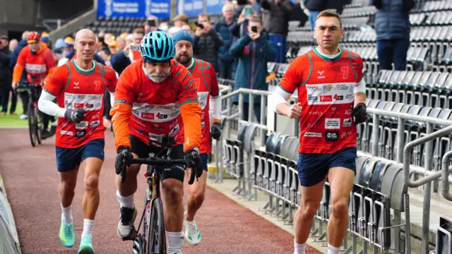 Kevin Sinfield, a cyclist and other runners at an athletics track