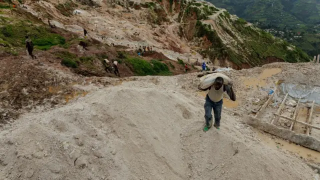 A labourer carries a sack up a steep sand bank at a mine