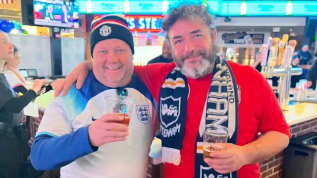 Two England football fans wearing white and red shirts and holding pints of beer