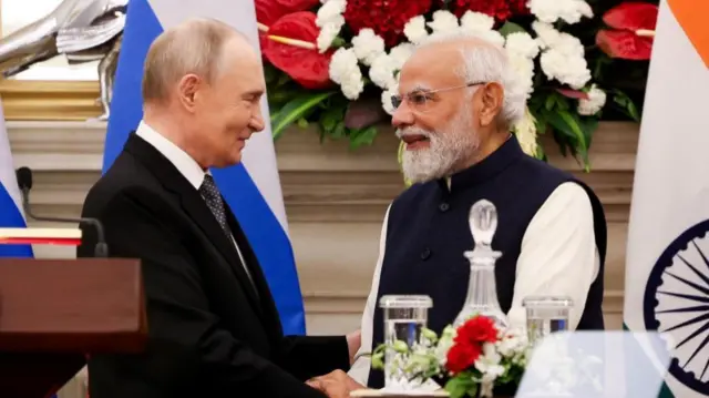 Putin and Modi shake hands standing next to a wooden podium