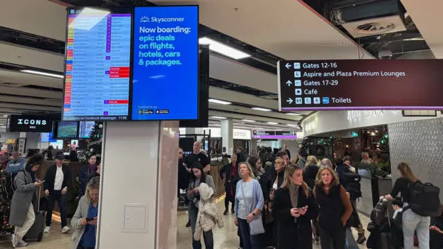 People walking through an airport with cancellations shown on a departures board
