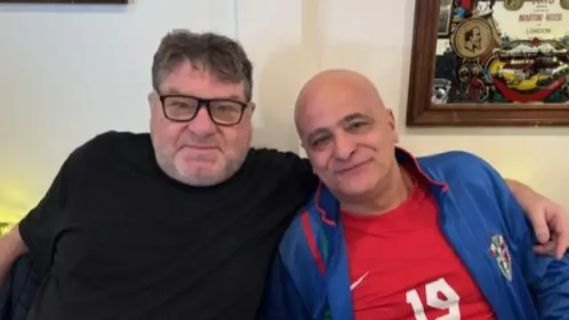 A man in a black shirt and a man in a blue jacket and red shirt