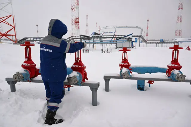 A man bundled up in a blue snowsuit as he turns red levers in the snow