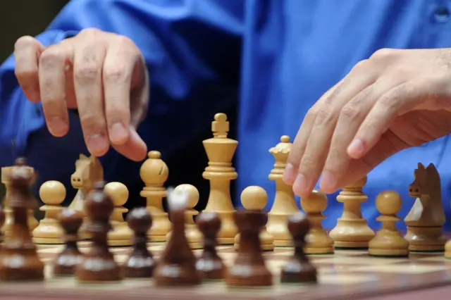 The hands of man weating a blue shirt near the white pieces on a chess board