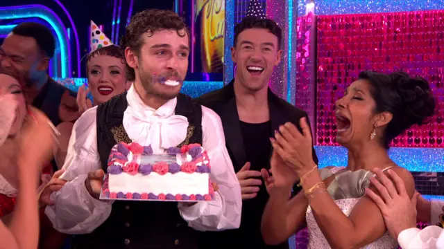George Clarke holding a birthday cake with some on his face