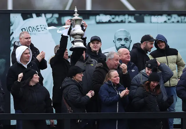 Boreham Wood fans celebrate their side's second goal against Newport by lifting a replica of the FA Cup