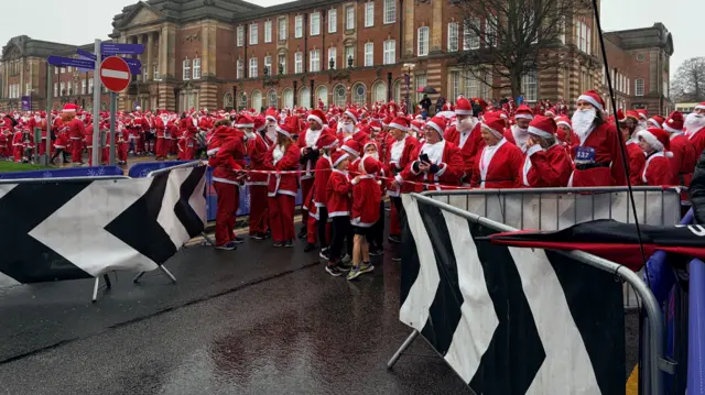 Hundred of people in Santa outfits stand behind barriers