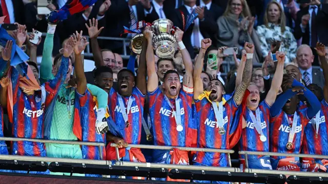 Former Crystal Palace captain Joel Ward lifts the FA Cup with his team-mates celebrating either side of him