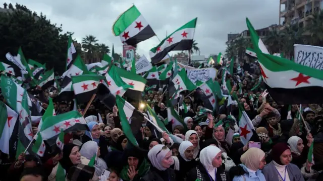Syrians gather in thick crowds to wave flags as evening descends