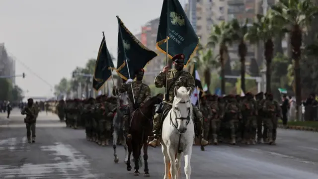 A man in a camouflage military outfit with a beret and sunglasses on is seen riding a horse and carrying a flag during the parade