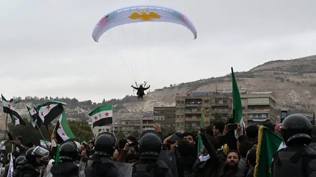 A paraglider is seen flying over crowds of people waving Syrian flags in Damascus