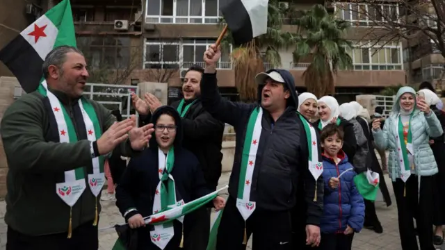Syrian men, women and children, wearing coats and scarves adorned with the Syrian flag, cheer and smile during a parade