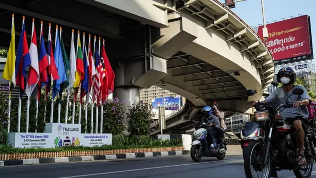 Flags of South East Asian countries perched on a podium beside a road