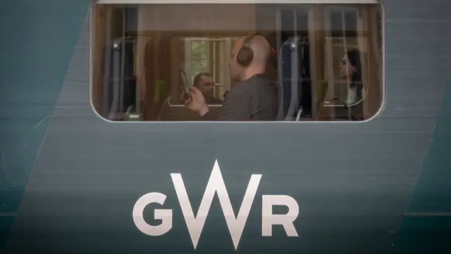 An image taken outside a train marked 'GWR'. A man can be seen through a window seated inside