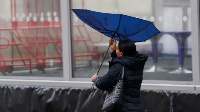 A woman holds a blue umbrella that has turned inside out