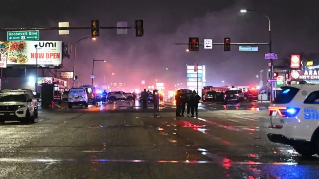 Staring down a busy street, there is a fire in the distance, and lots of police cars parked with police officers stood around in groups