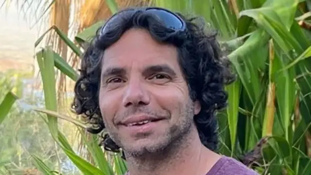 Ofer Kalderon with sunglasses on head, smiling, with plants behind him